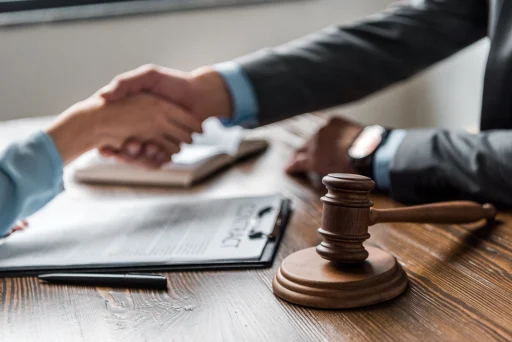 Close-up view of wooden hammer and lawyer with client shaking hands behind